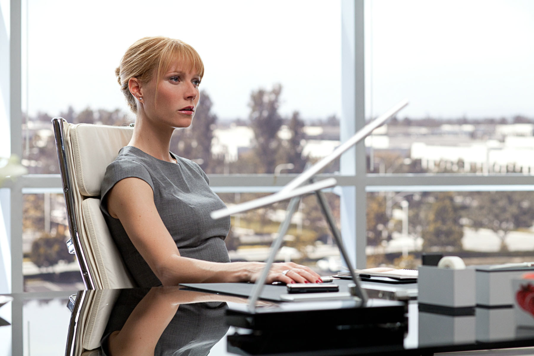 sharply dressed with her hair in a neat bun, Pepper sits at her CEO desk