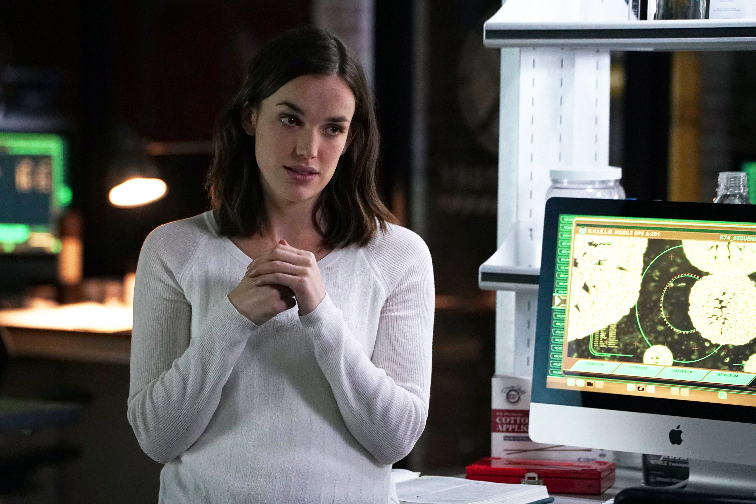 wearing a soft, long-sleeves shirt, Simmons leans against her computer desk and wrings her hands