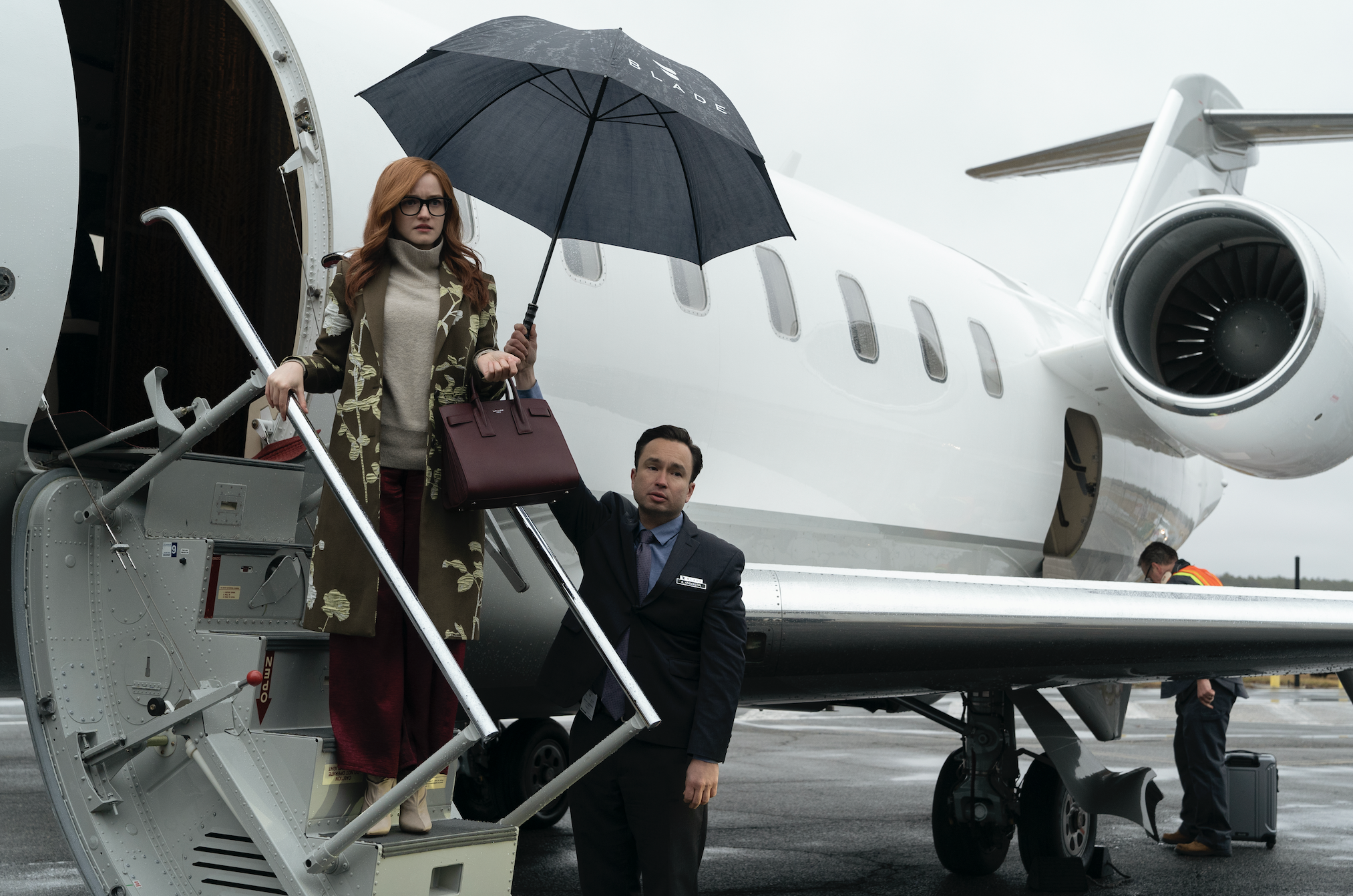 A red headed woman with a man holding an umbrella over her head boarding a jet