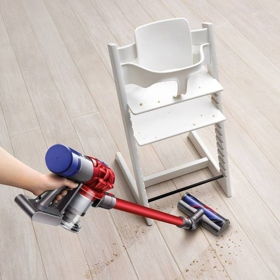 model using the cordless stick vacuum to vacuum crumbs under a high chair