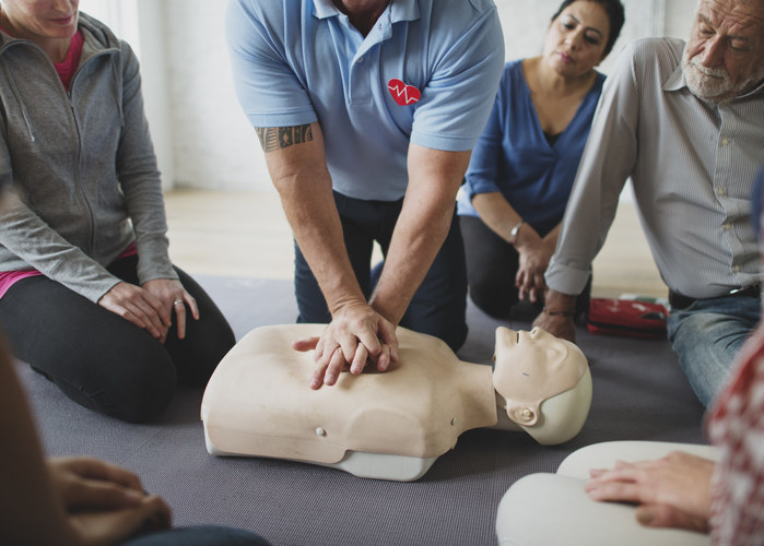 Someone performing CPR on a dummy in front of a group