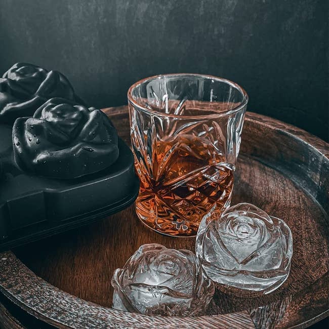 two ice cubes shaped like roses on a tray next to a glass of whiskey