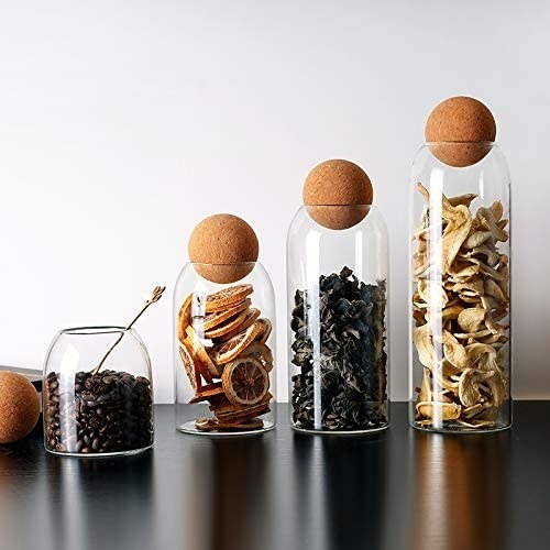 four glass containers with cork balls on top