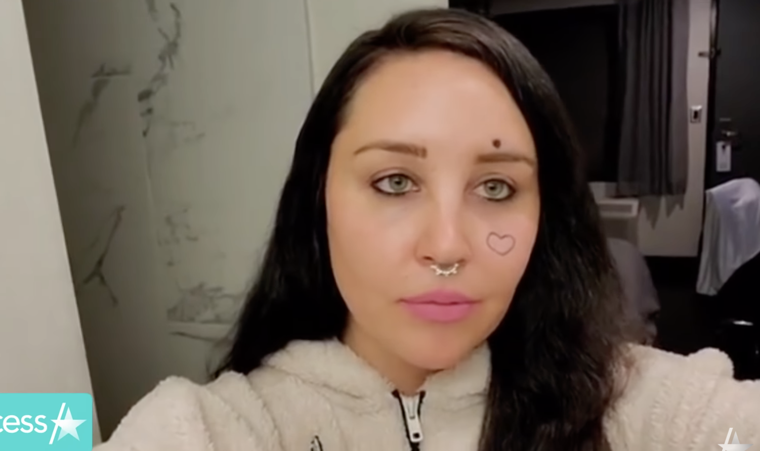 A selfie of Amanda Bynes with dark hair and a heart tattooed on her face