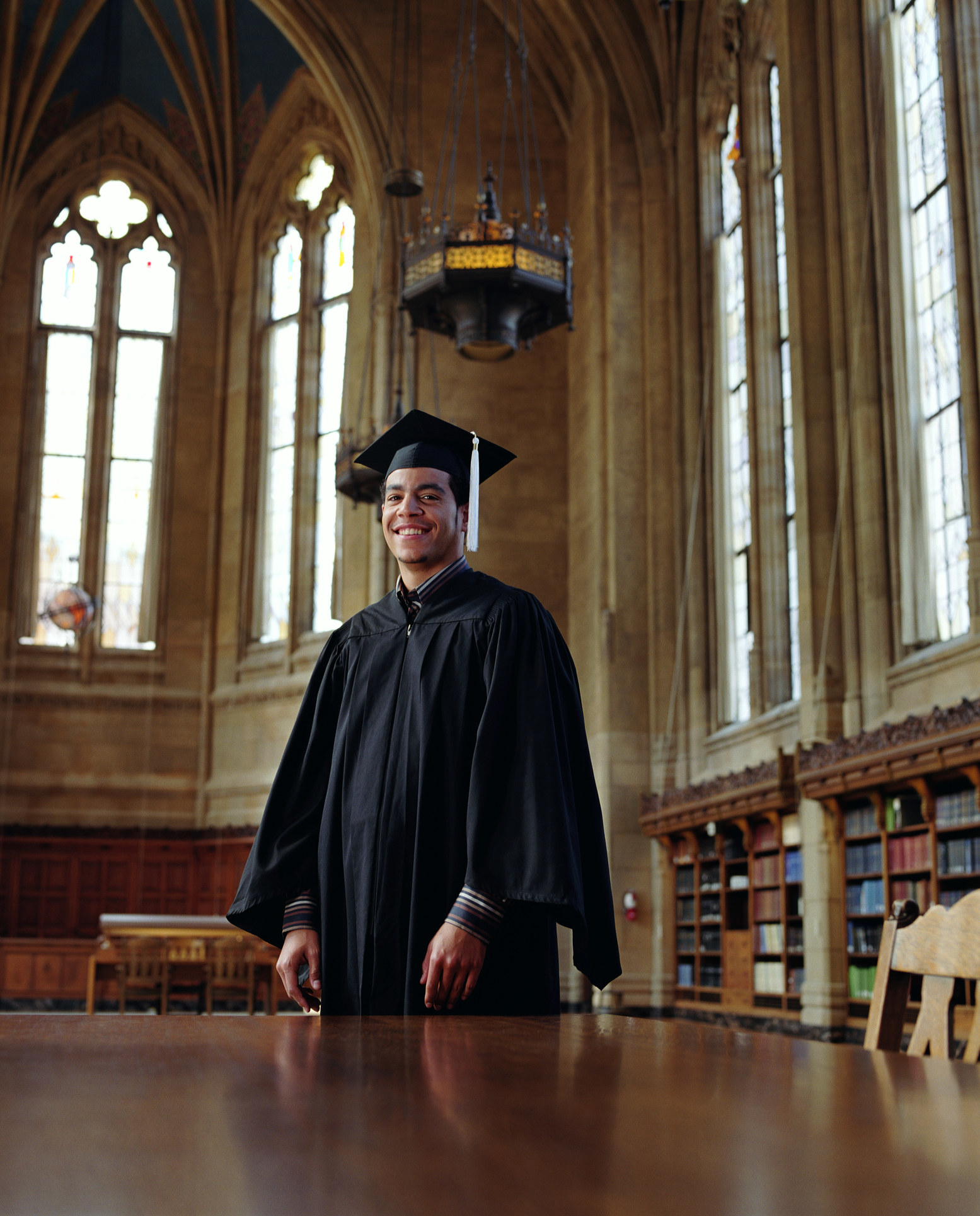 Young man in cap and gown smiles in his graduation robe in the university library