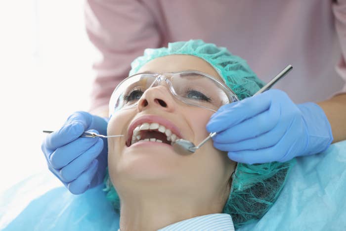 Periodontist using tools in a woman&#x27;s mouth while she wears goggles and a hairnet