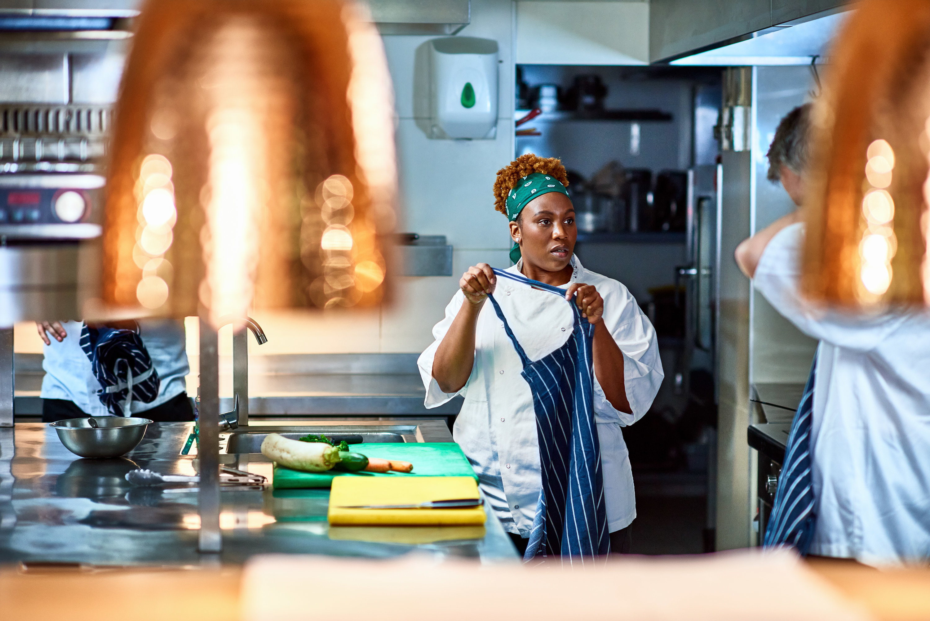Woman puts on apron in restaurant kitchen and listens to colleague