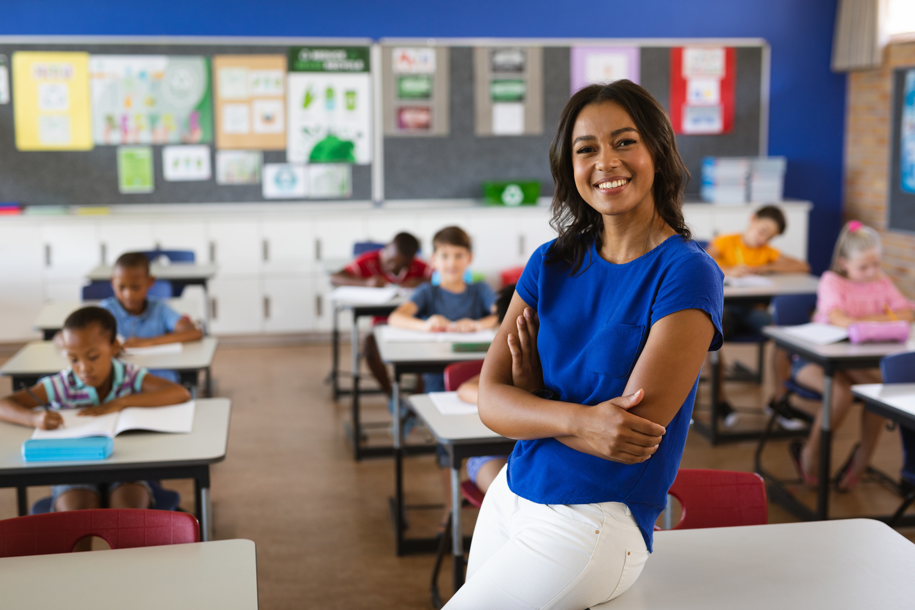 Teacher smiling in a classroom with students in the background