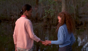 A woman and a girl hold hands and look into a body of water