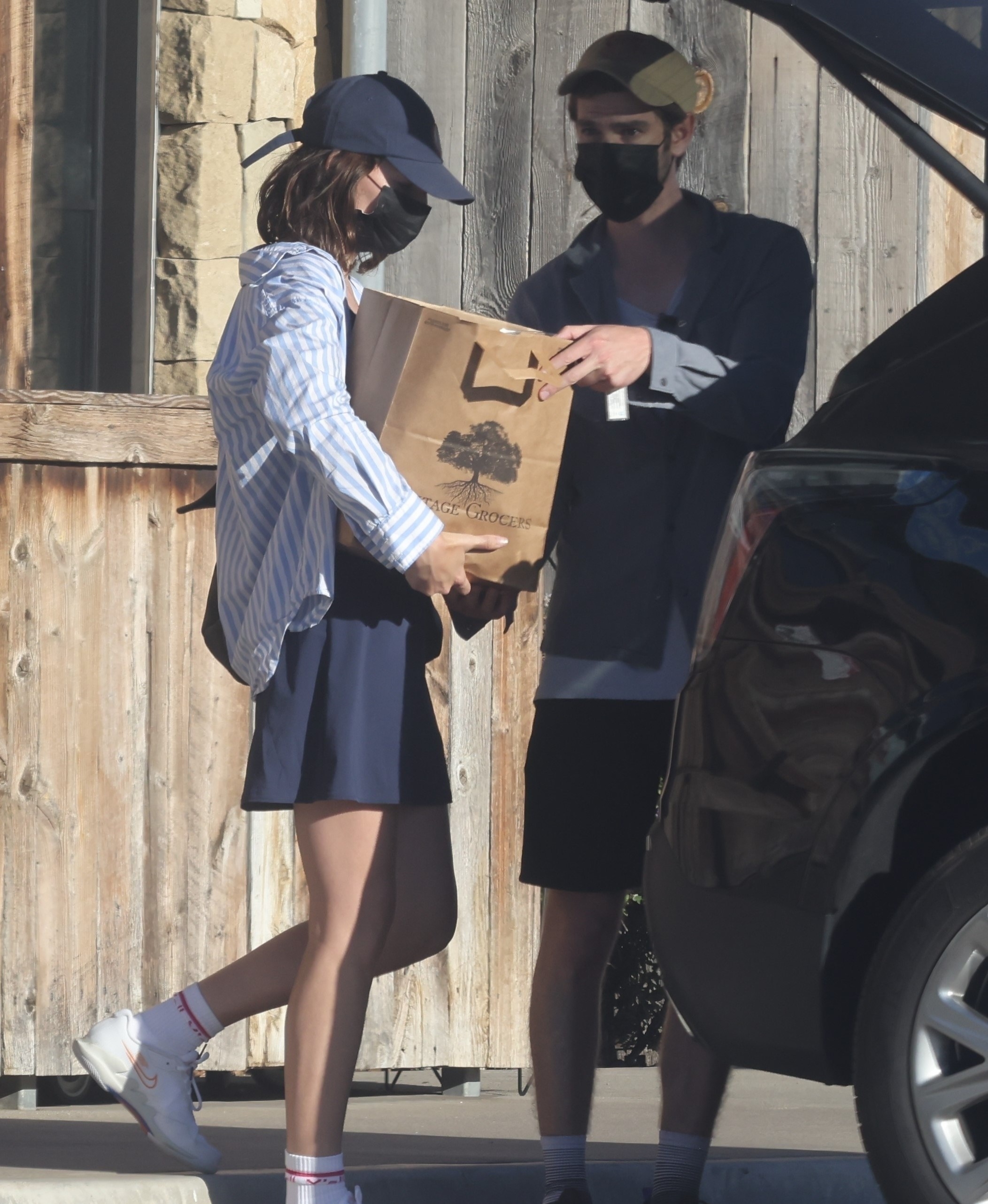 Alyssa hands Andrew a paper grocery bag, which he loads into the car