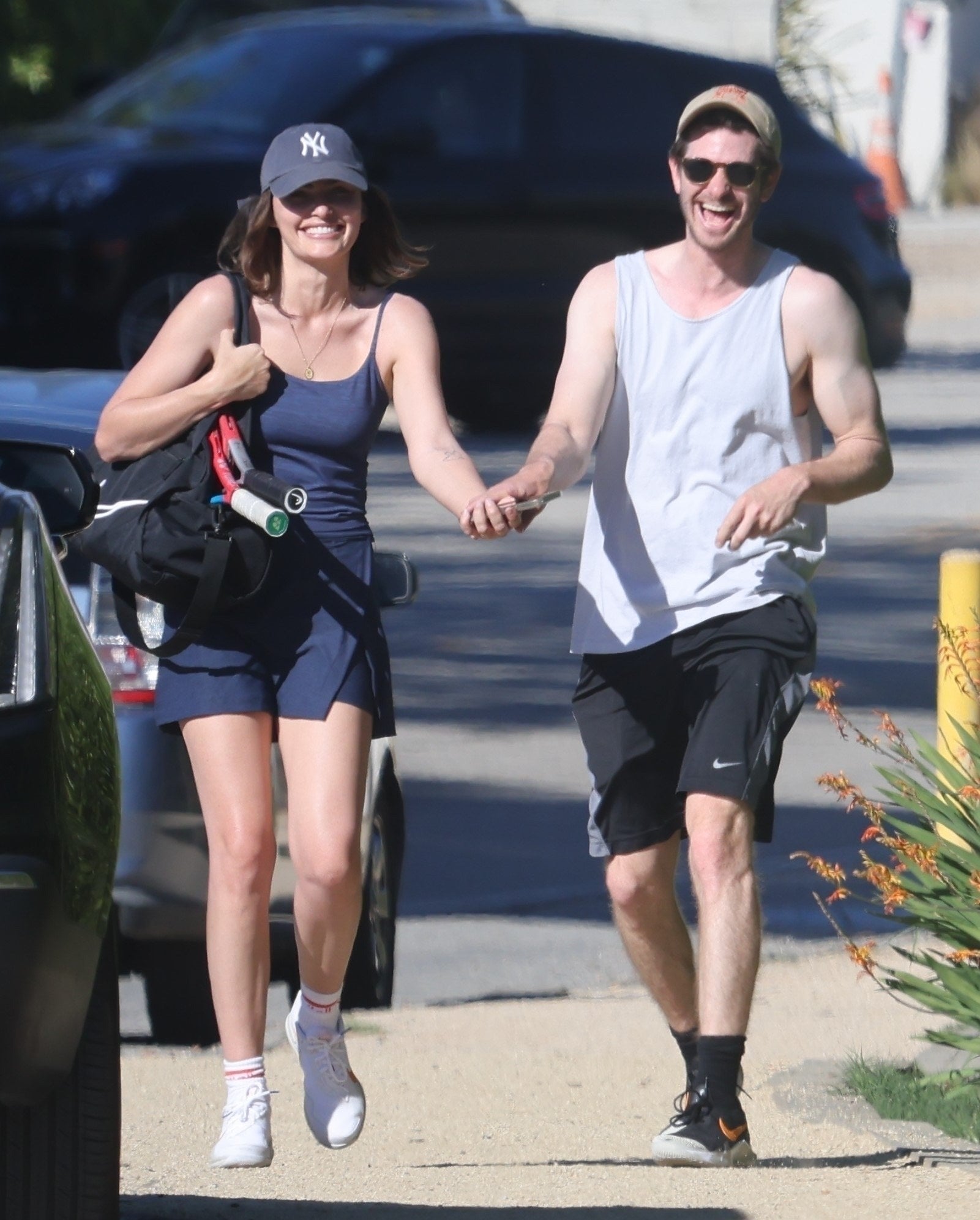 wearing workout clothes, they hold hands and laugh while jogging down the street
