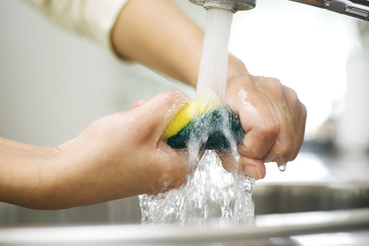 A person holding a kitchen sponge underneath running water