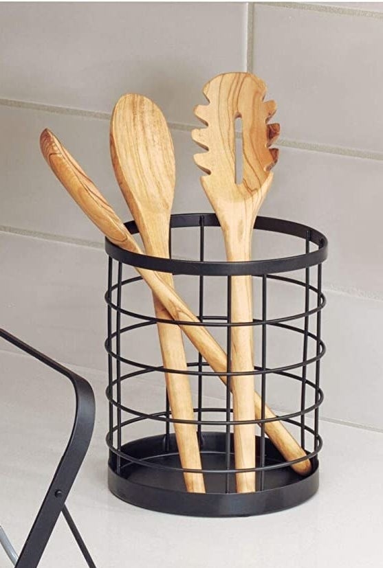 The wire basket on a kitchen counter with three wooden kitchen utensils in it