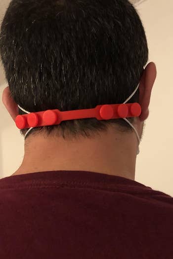 A reviewer wearing a mask that is pulled together around the back of their head by the silicone ear saver, which has three different toggles on the back for sizing