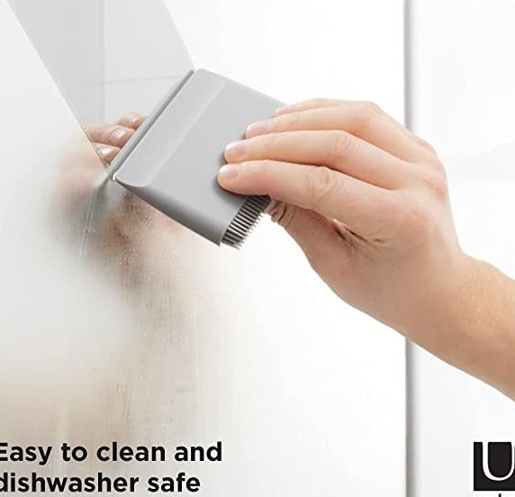 A person&#x27;s hand using the squeegee to wipe fog away from a mirror in a bathroom