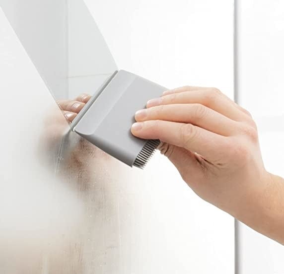 A person&#x27;s hand using the squeegee to wipe fog away from a mirror in a bathroom