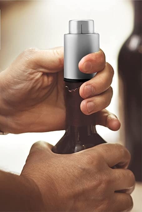 A person placing the wine stopper on a bottle of wine