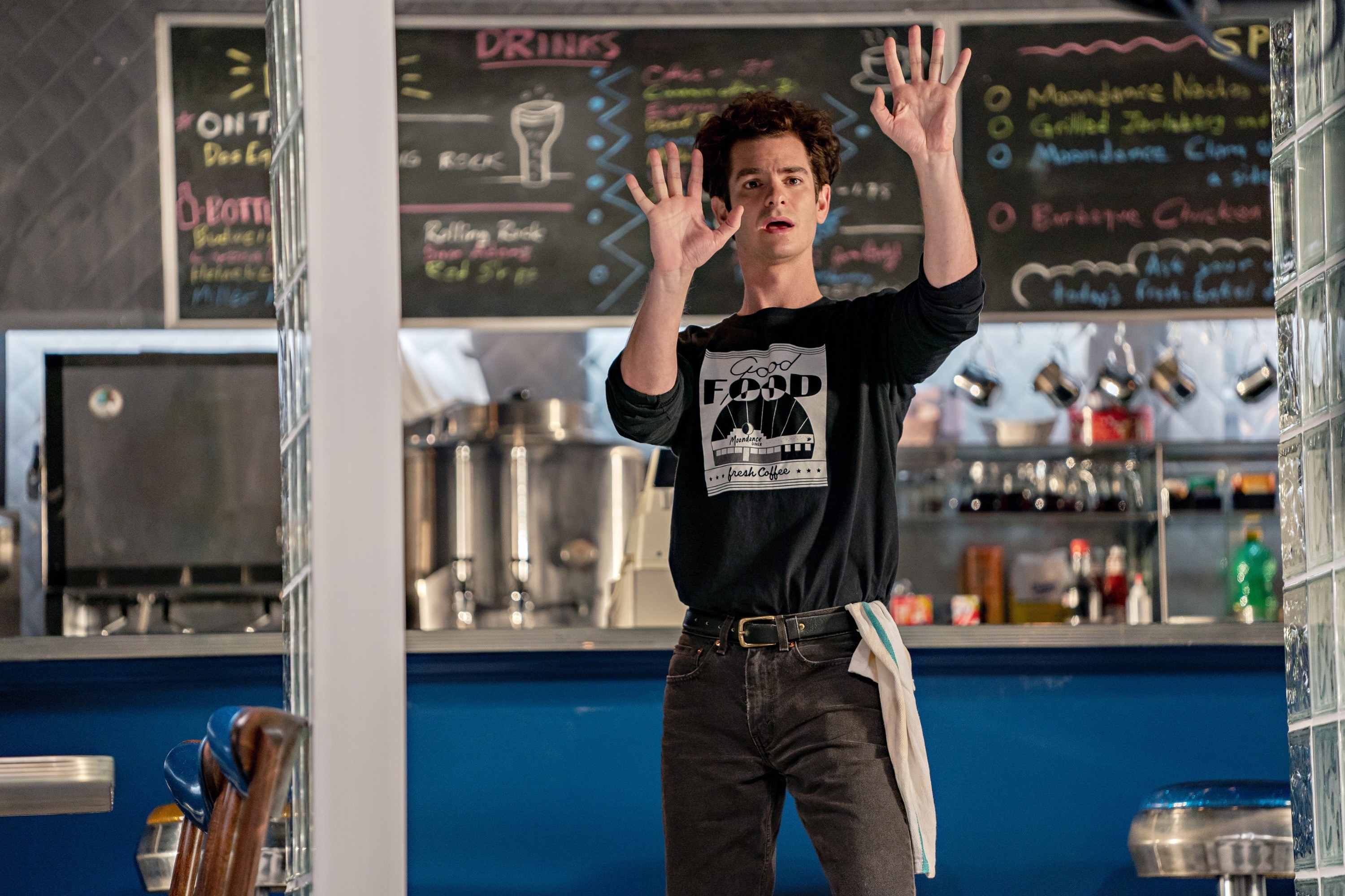 Andrew Garfield stands in a diner