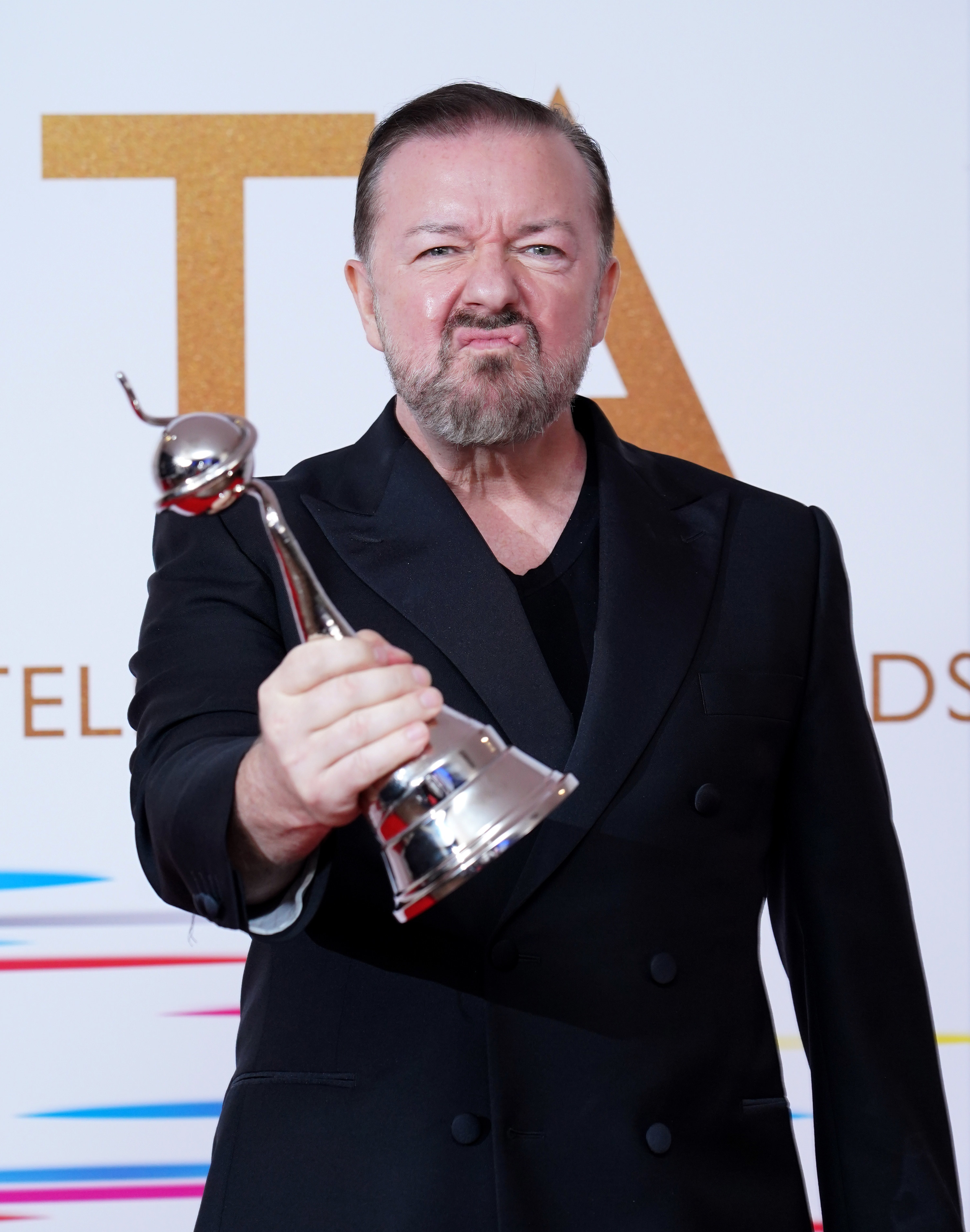 Ricky Gervais making a face at the camera while clutching a National Television Award in his hand