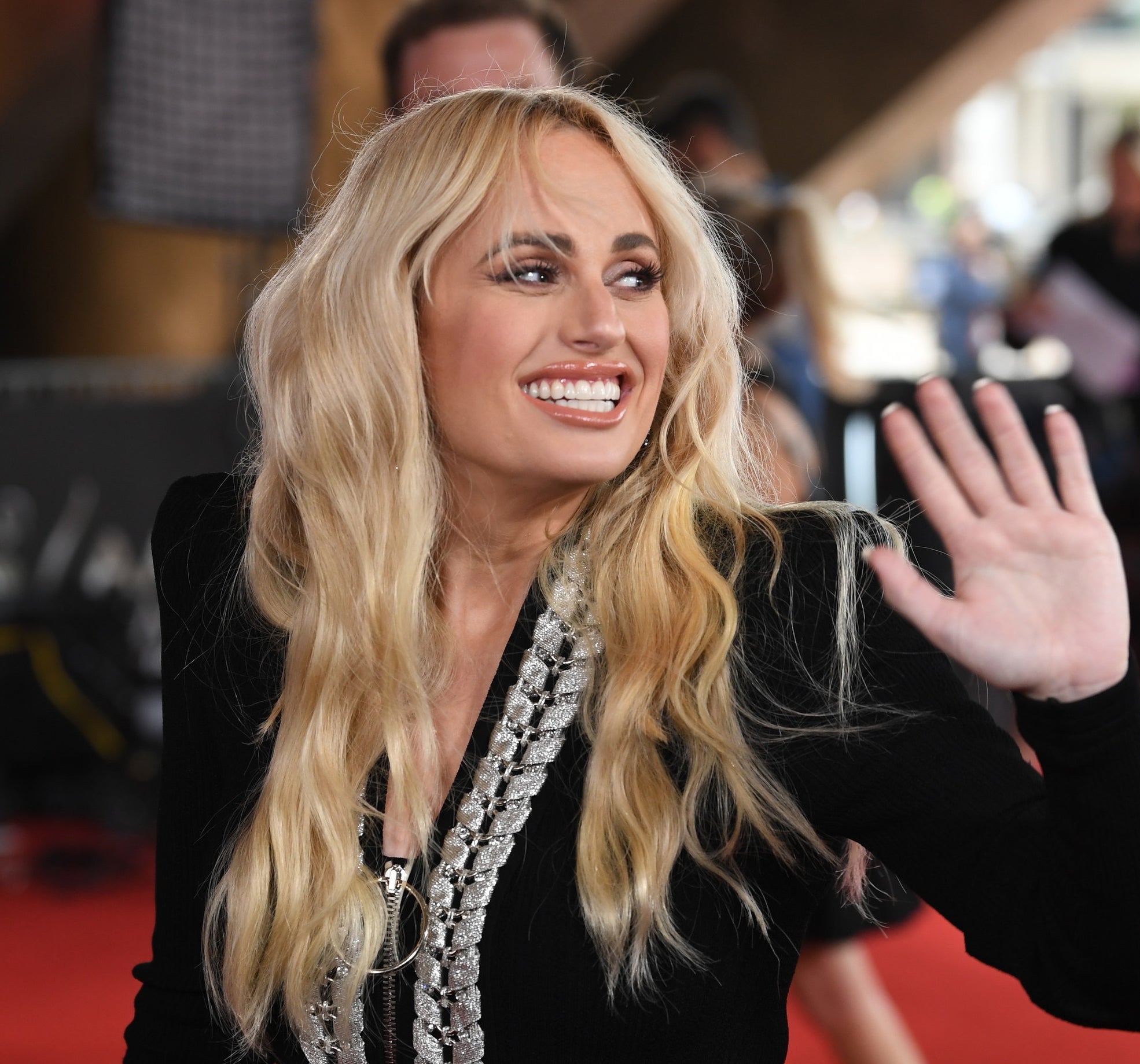 Rebel Wilson in a long-sleeve dress with long wavy hair smiling and waving at the 2021 AACTA Awards