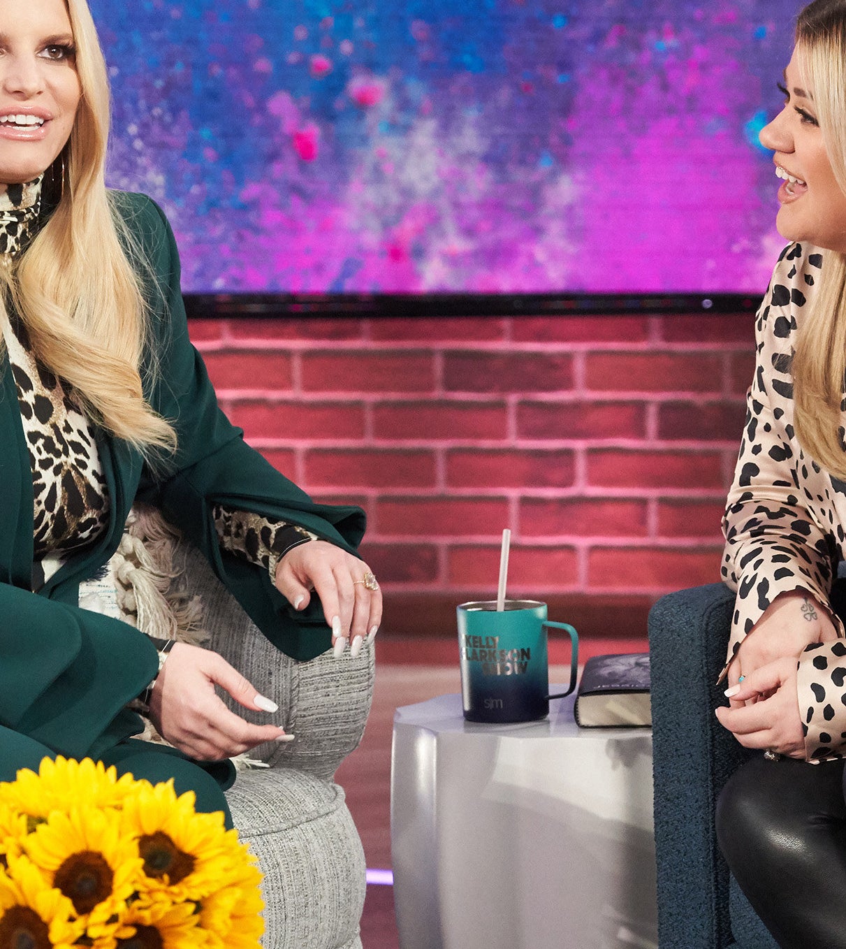 Jessica Simpson sitting on a couch in a long-sleeved dress with a bouquet of sunflowers in front of her on &quot;The Kelly Clarkson Show&quot;