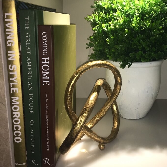 a reviewer photo of the gold sculpture being used as a bookend