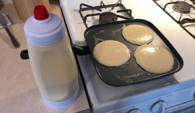 a reviewer's dispenser filled with batter next to a griddle pan with pancakes cooking on it