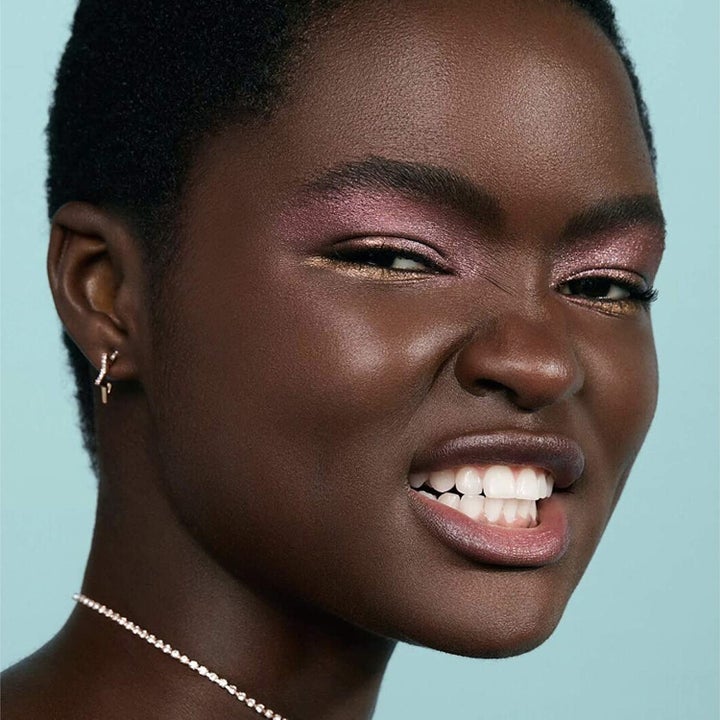 dark-skinned model wearing a shimmery pink-purple shade on their eyelids and a shimmery gold shade under their eyes