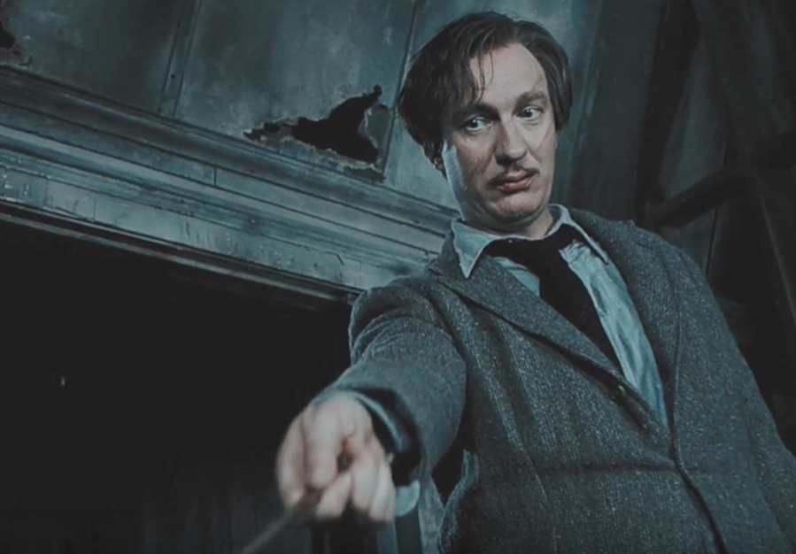 remus lupin wears a sweater over a button-down shirt and tie, holding a wand