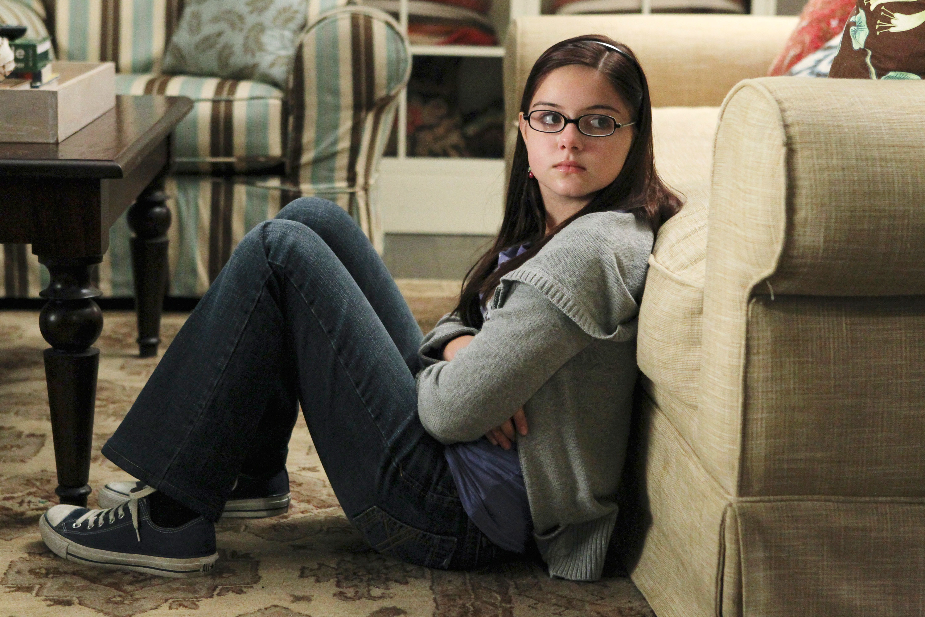 Teen girl sitting on floor in Converse, leaning against couch and looking moody