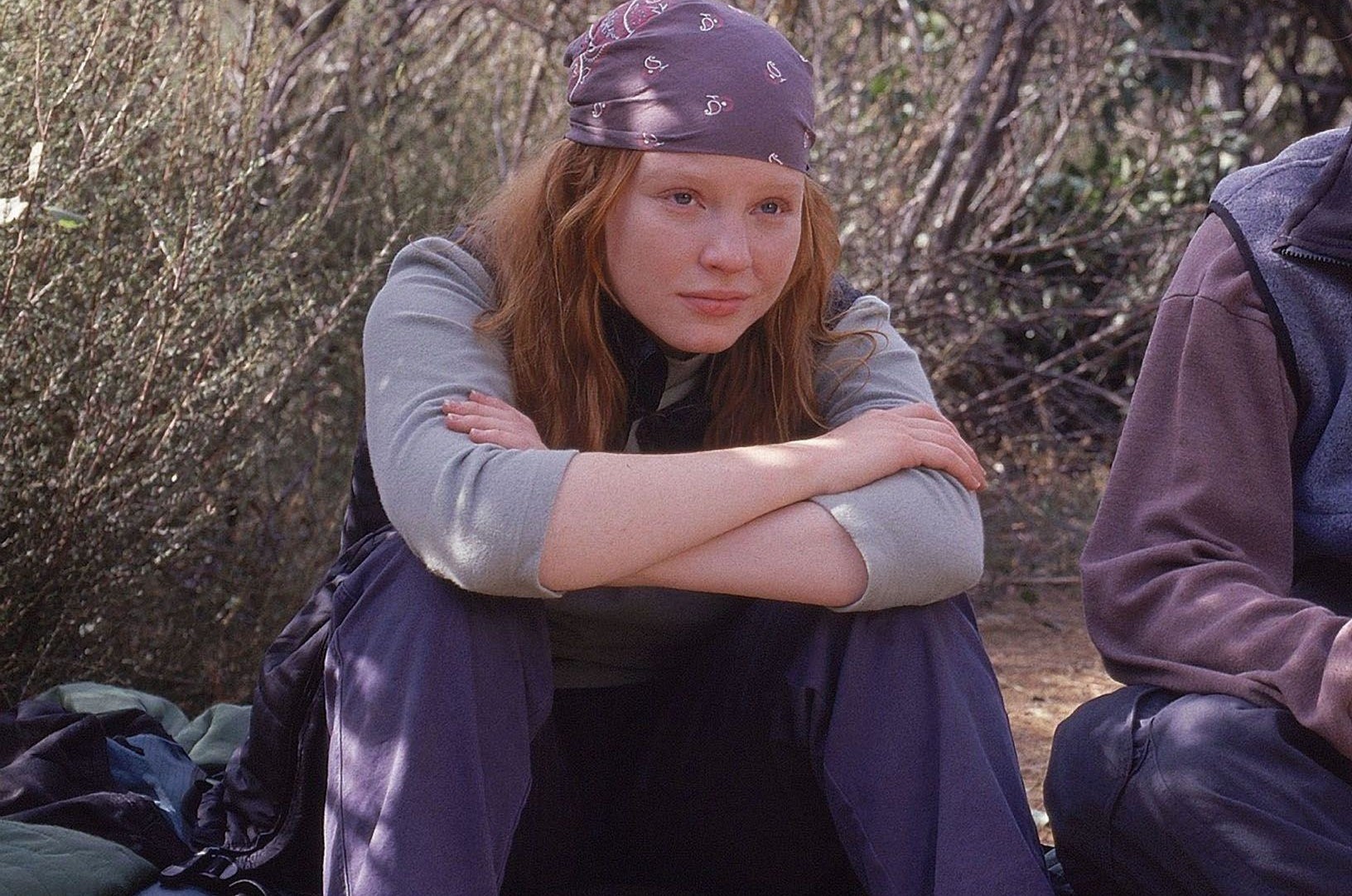 Teen girl sitting down wearing a bandana outside with arms folded