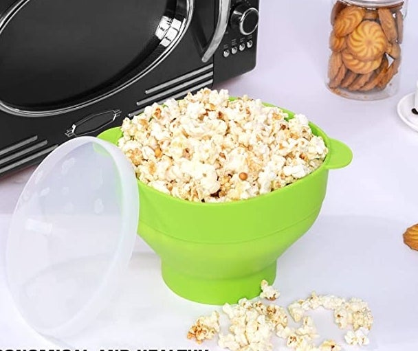 The popcorn maker on a counter filled to the brim with fresh popcorn, the clear plastic lid is leaning on the side