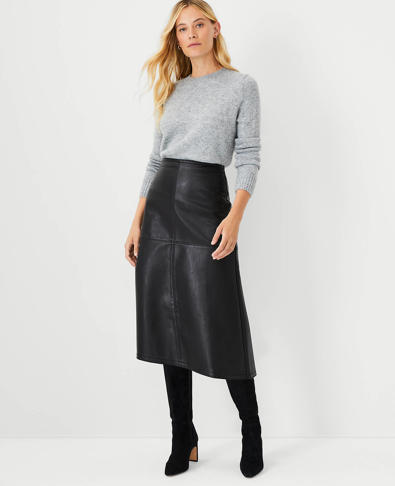 model wearing black faux leather skirt with knee high boots and gray sweater