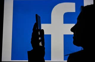 A woman looking at her phone in front of the Facebook logo