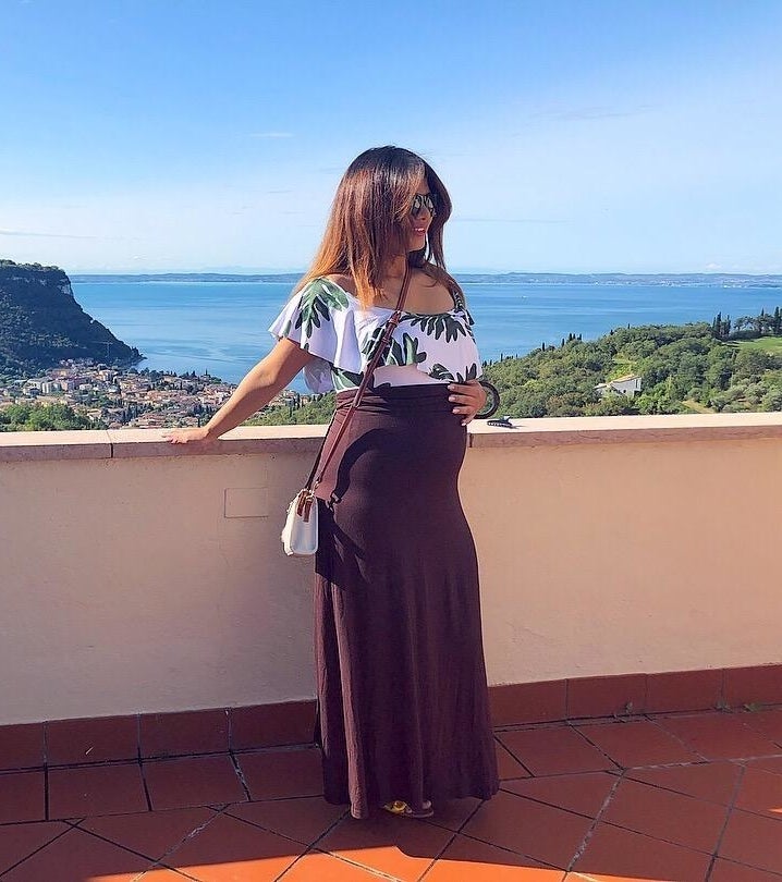 pregnant reviewer, leaning against a low wall with ocean view in background, wearing maroon maxi skirt