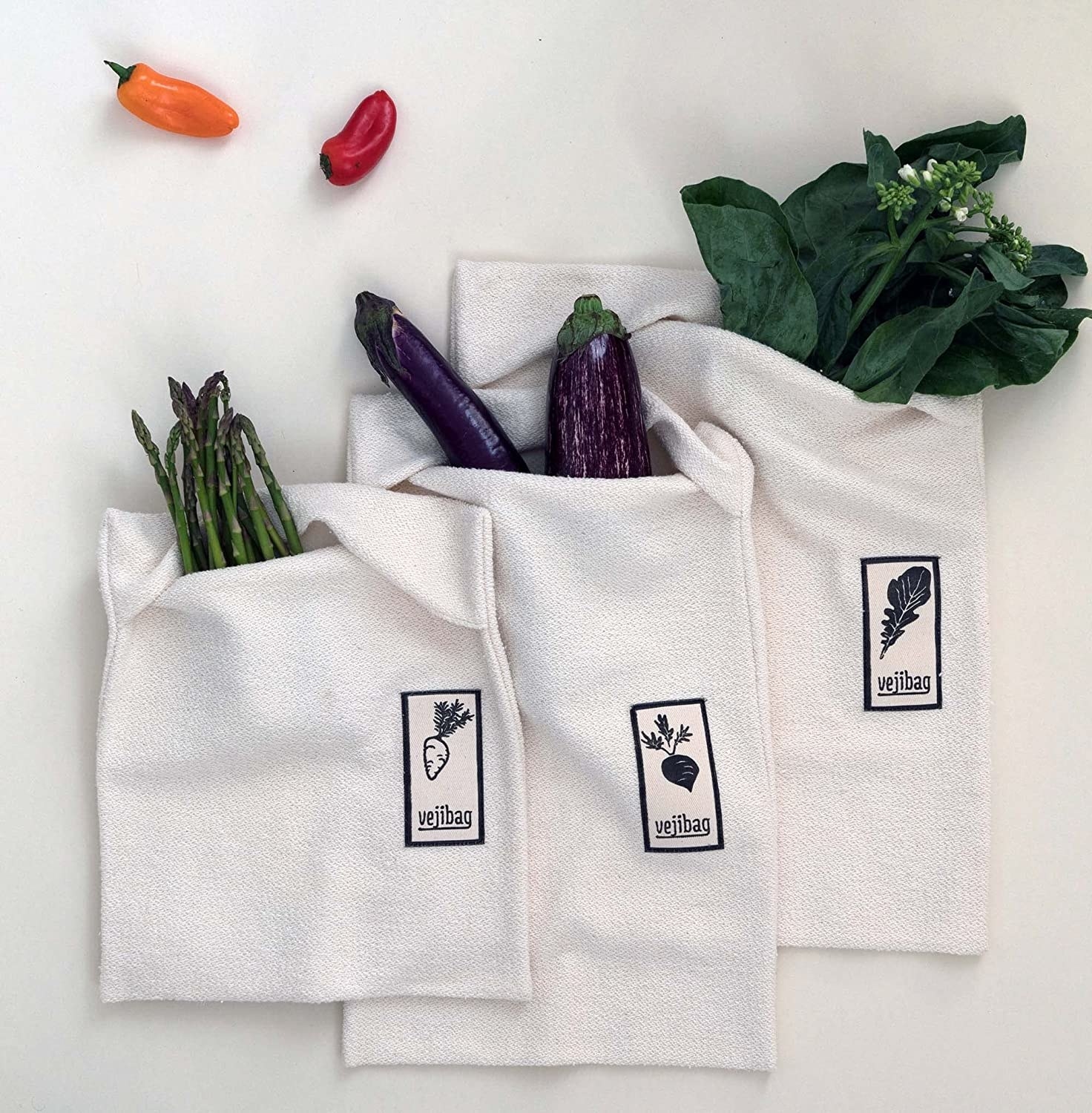 three organic cotton crisper bags holding asparagus, eggplant, and greens