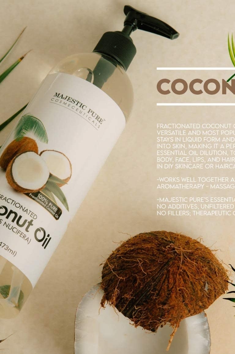 A bottle of coconut oil laying down surrounded by raw coconut and palm leaves
