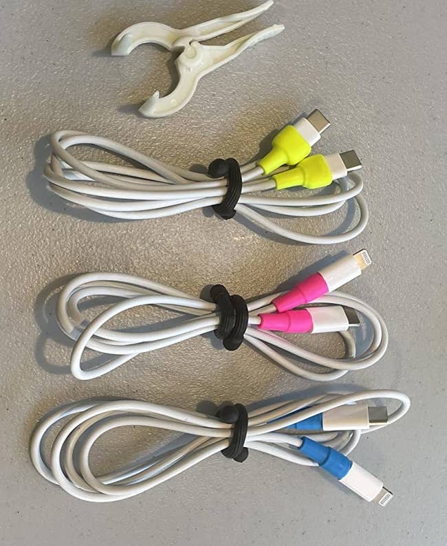 a reviewer photo of three different charging cords with the cord protectors installed on each end sitting next to the included applicator tool