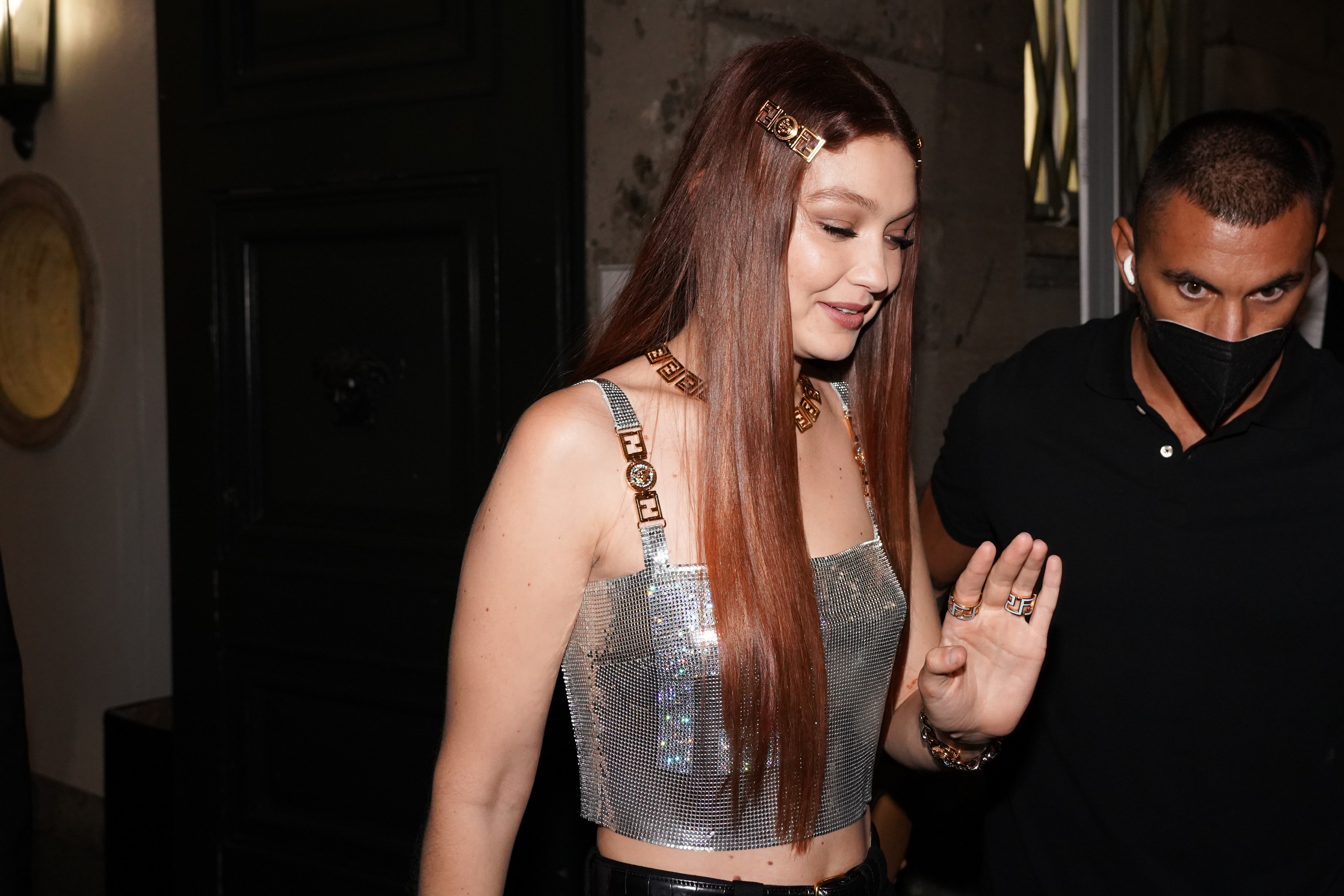 Gigi holds her hand up while leaving an event