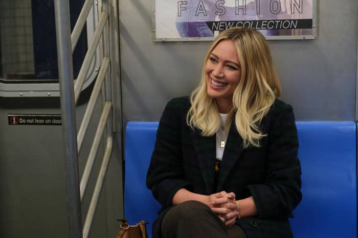 Hilary's character sits on the subway