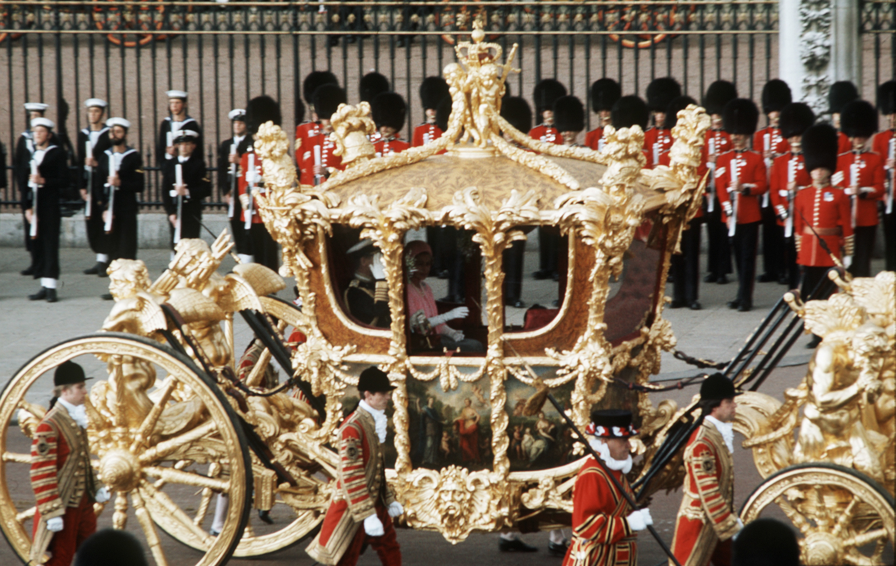 Queen Elizabeth II and price philip on a golden carriage with soldiers behind them 
