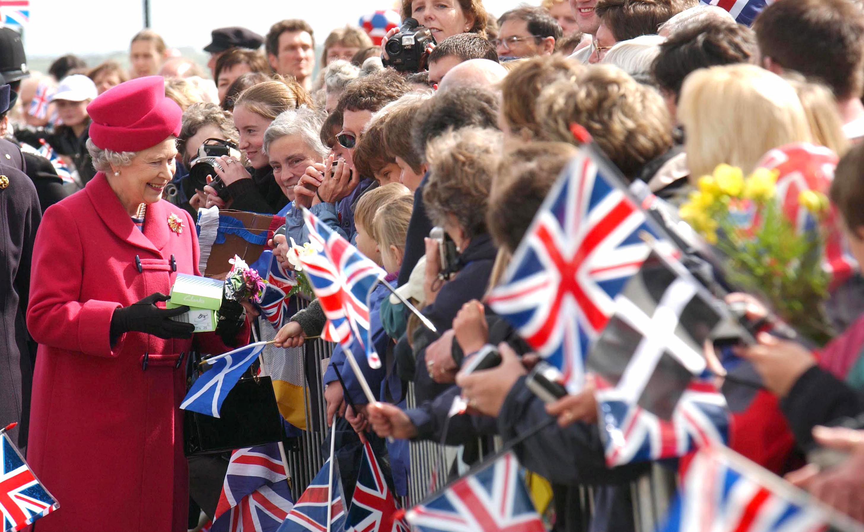 Queen Elizabeth II shaking hands and receiving gifts with a crowd of people in the stands