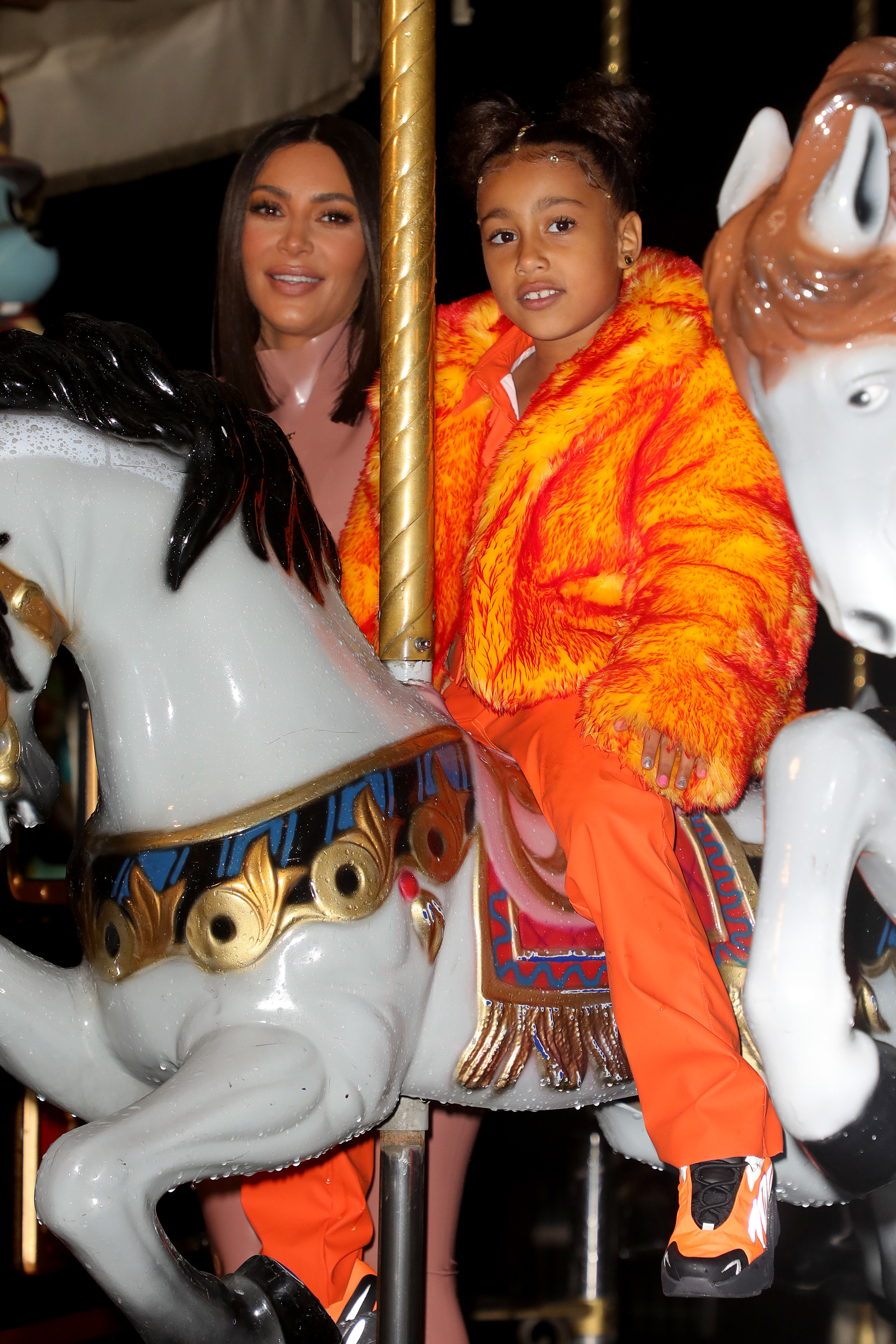 Kim standing next to North who&#x27;s riding a merry-go-round