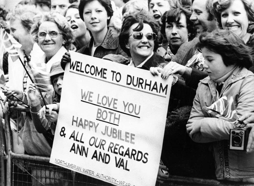 A woman holding a sign that says welcome to durham we love you both happy jubilee and all our regards ann and val