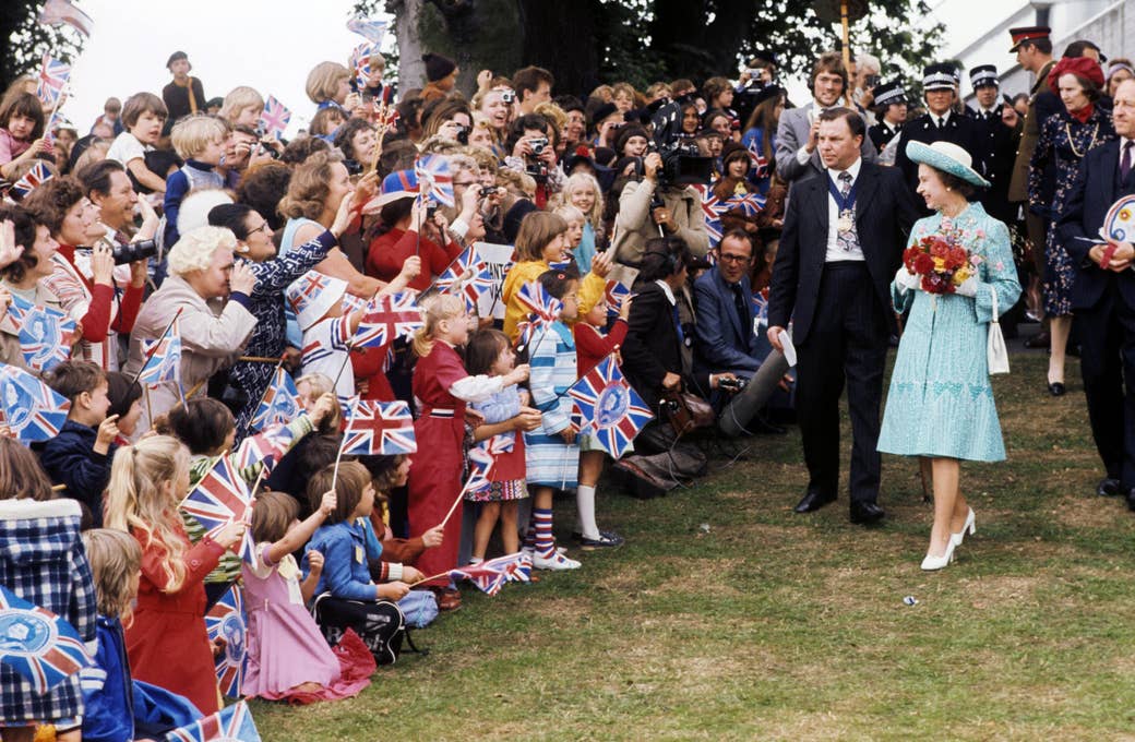 The queen walking in a blue dress past a bunch of people waving flags