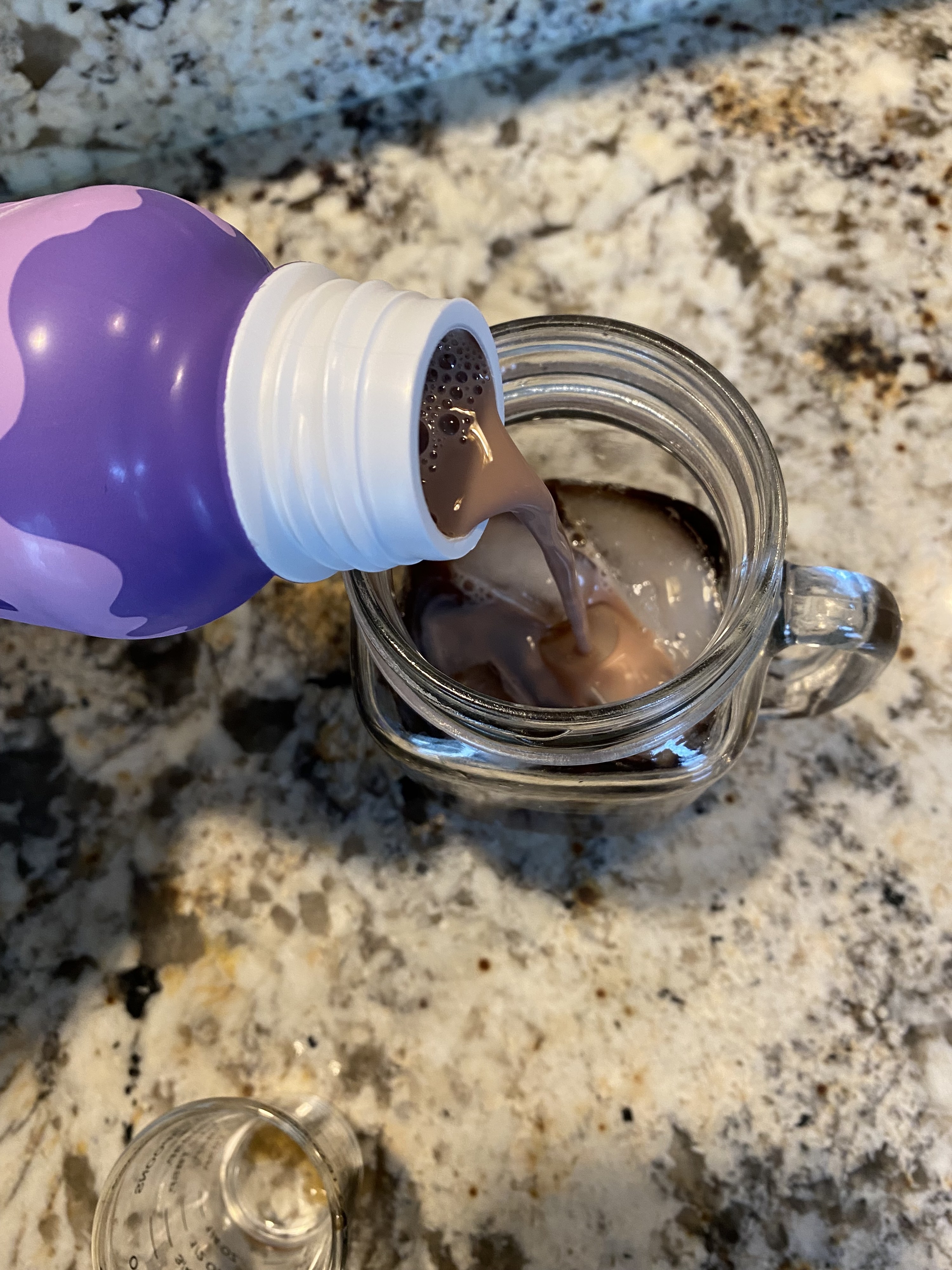 A bottle of a chocolate protein shake being poured into a glass of iced coffee