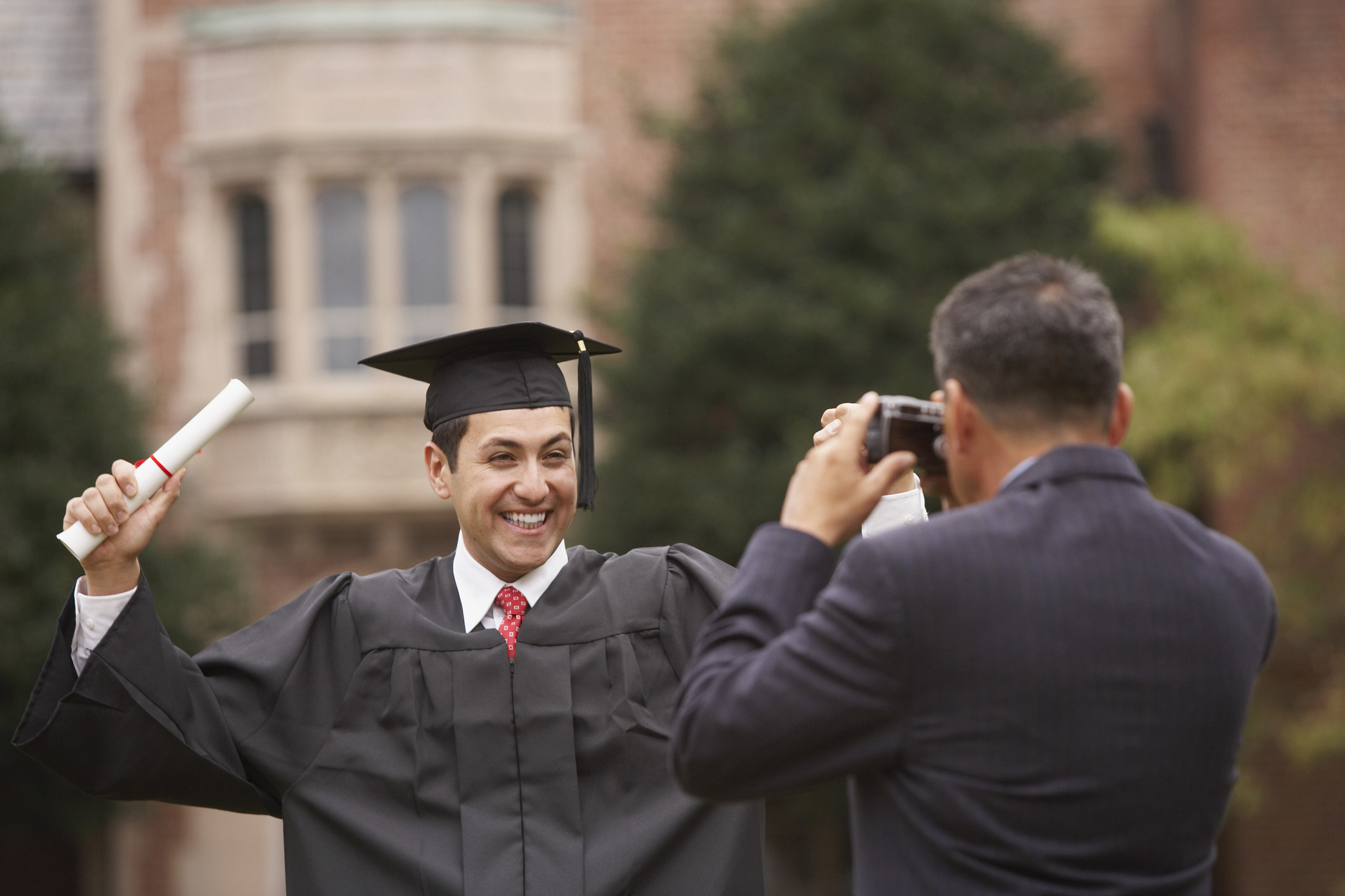 An excited college grad poses while their parent takes a photo