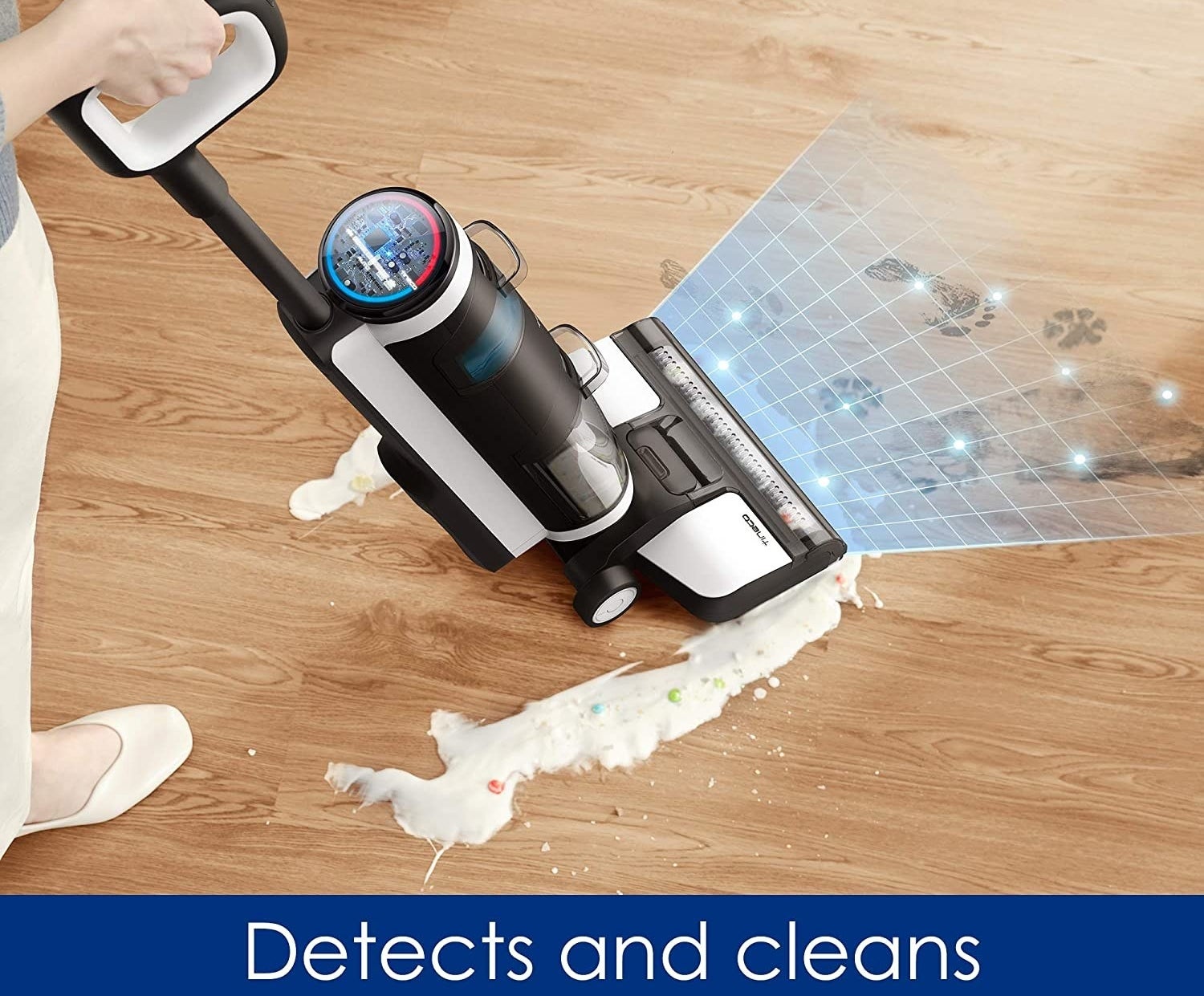 A person cleaning spilled cereal and muddy pawprints off a wooden floor with a vacuum
