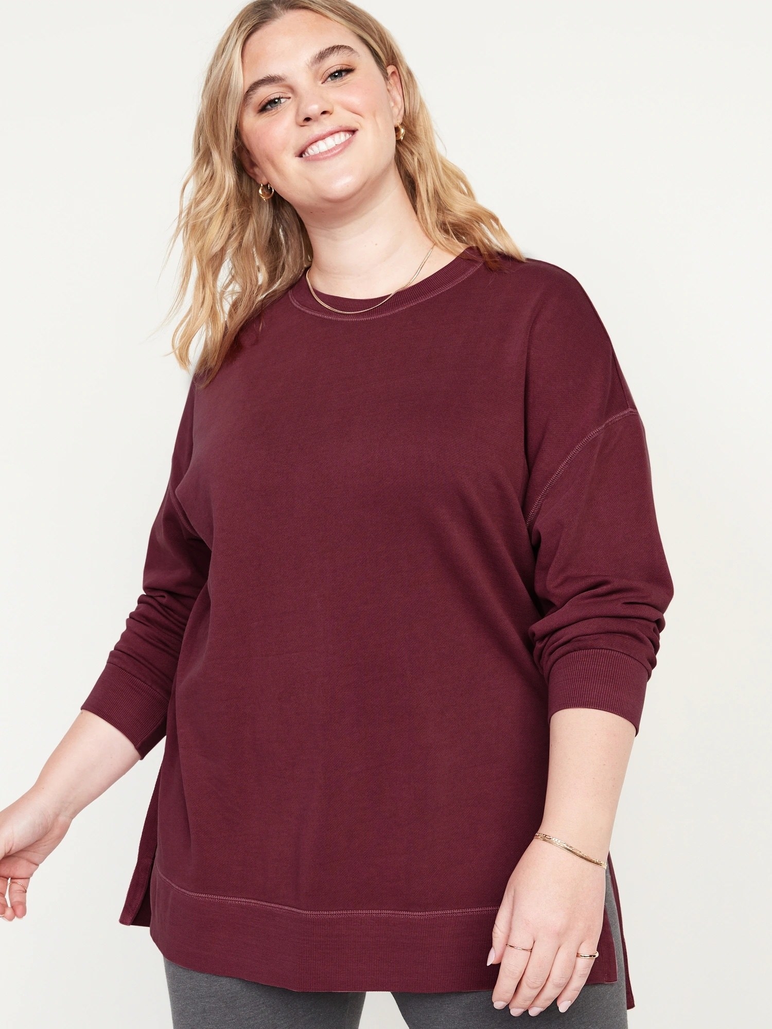 A person wearing the sweater over a pair of leggings in front of a plain background