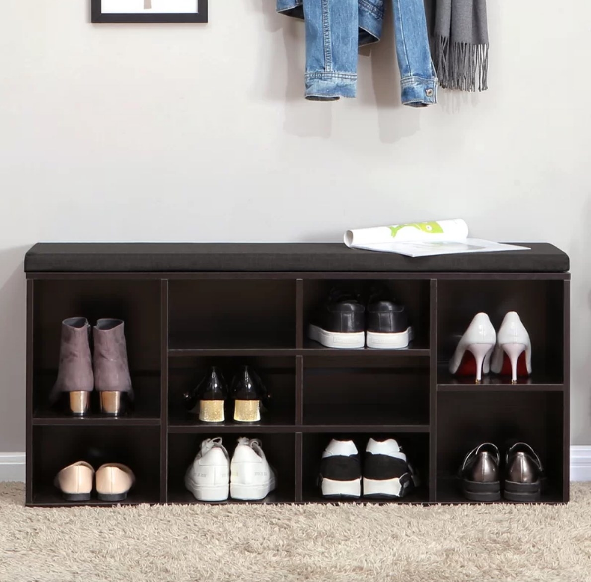 Dark brown shoe bench with shoes in underneath cubbies, black cushioned bench top